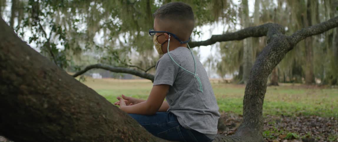 Young boy wearing a face mask sitting on a tree branch in the park