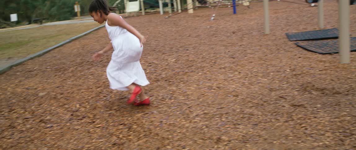 Girl in a white dress jumps off a swing on a playground in a park