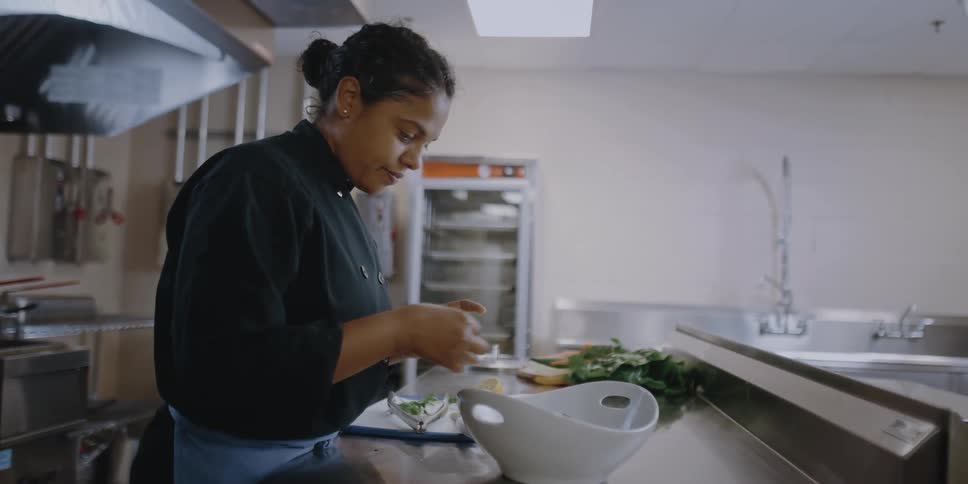A female chef places vegetables in a bowl in an industrial kitchen