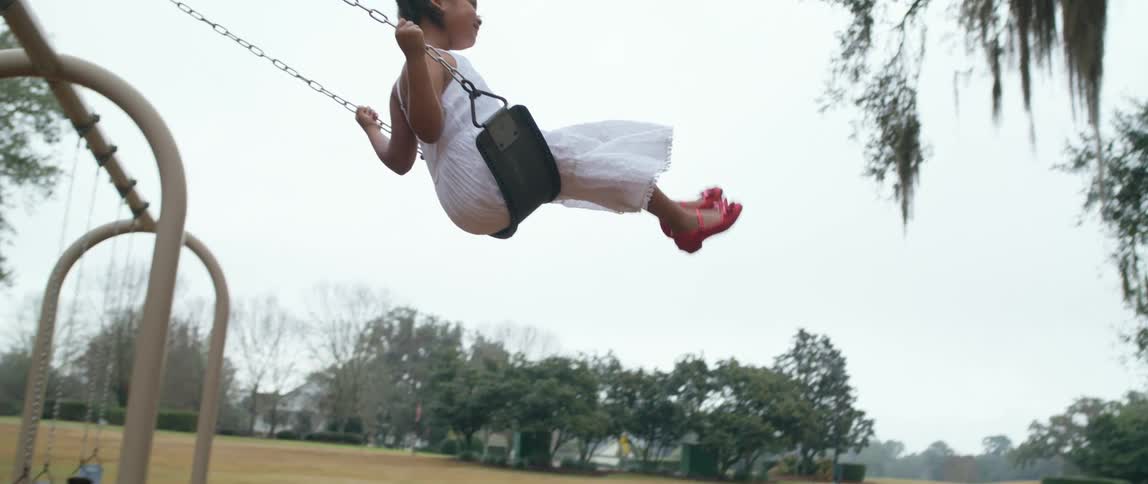 Kids are swinging in a public park play area as a parent supervises