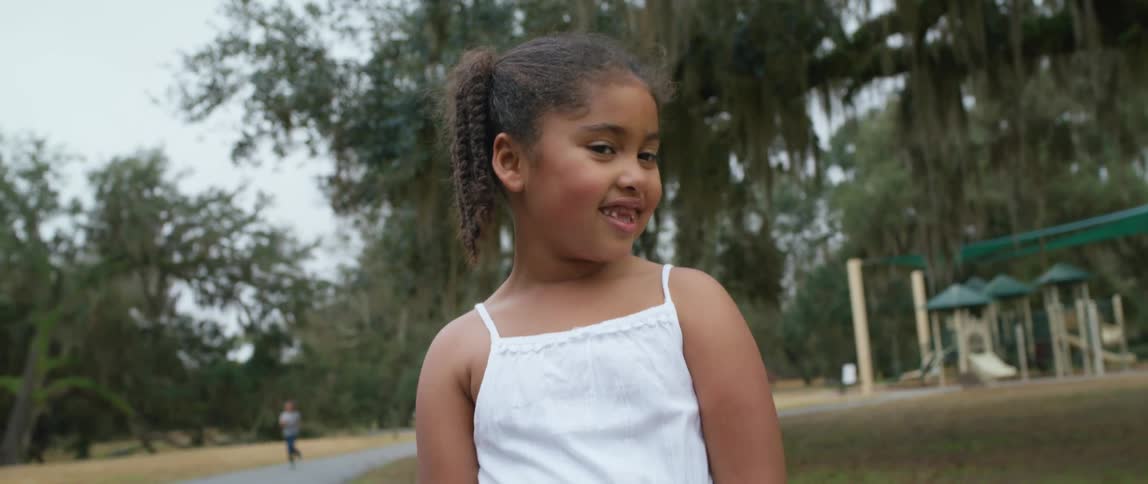 A young girl stands at a public playground and smiles