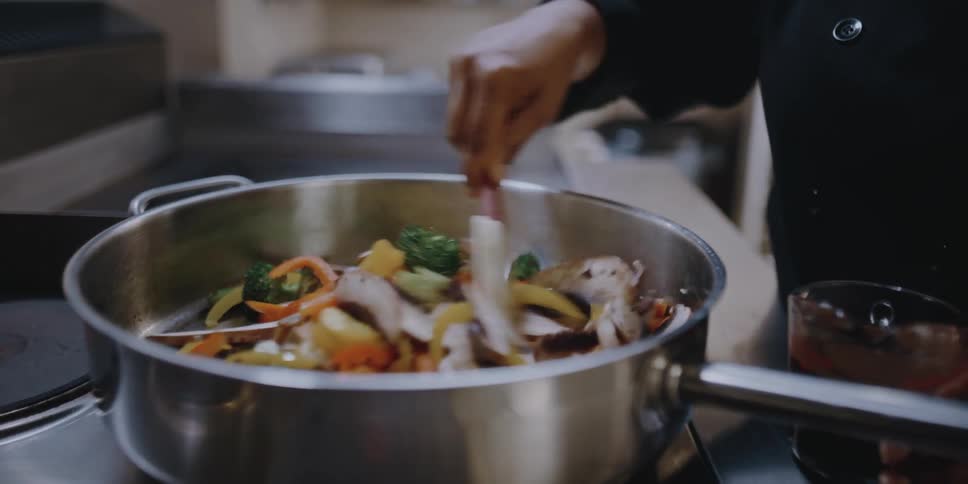 Female chef cooking vegetables on a pan in the kitchen of a restaurant