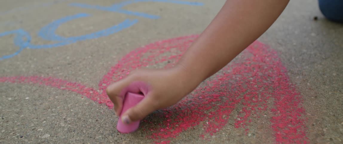 A child drawing a heart with pink chalk on the sidewalk