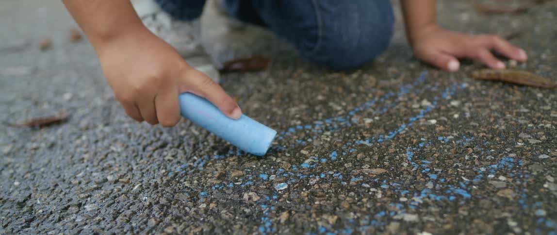 A young child draws on a sidewalk with chalk