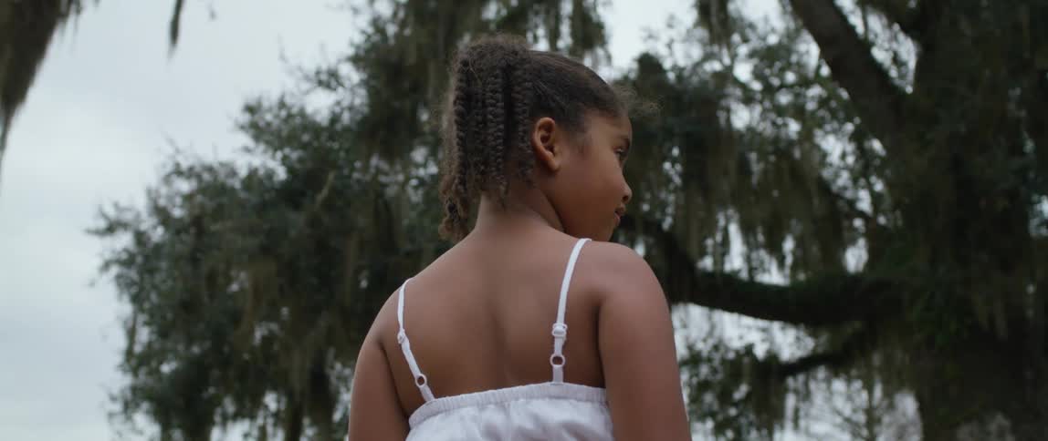 A girl looks around at her surroundings while stand under a large tree outdoors during the day