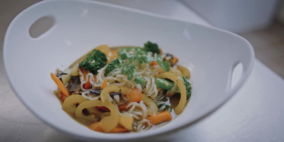White bowl full of noodles and vegetables sits on white table