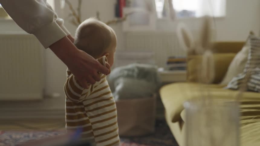 A mom holds her sons hands as he takes his first steps