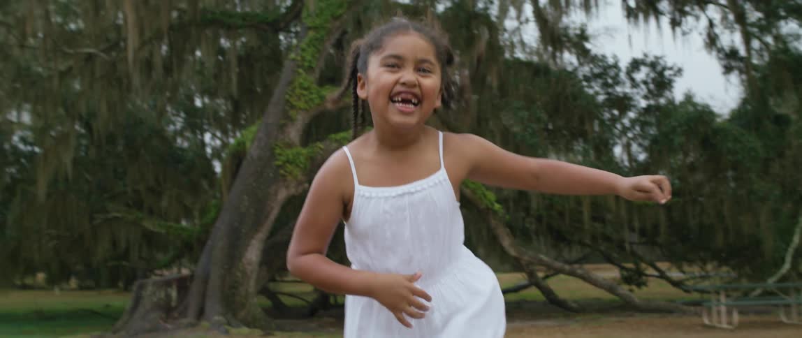 Happy girl in a white dress dancing and smiling near the trees outdoors