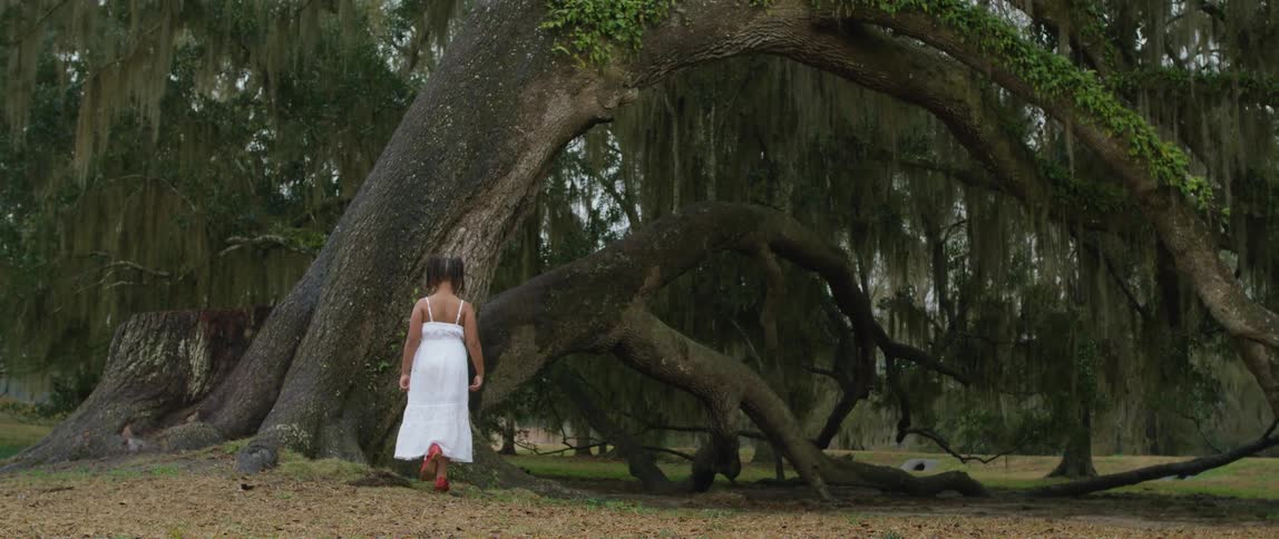 Girl wearing a white dress and red shoes walking towards the trees
