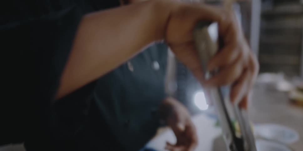 A woman uses tongs to adjust the food presentation in a restaurant bowl