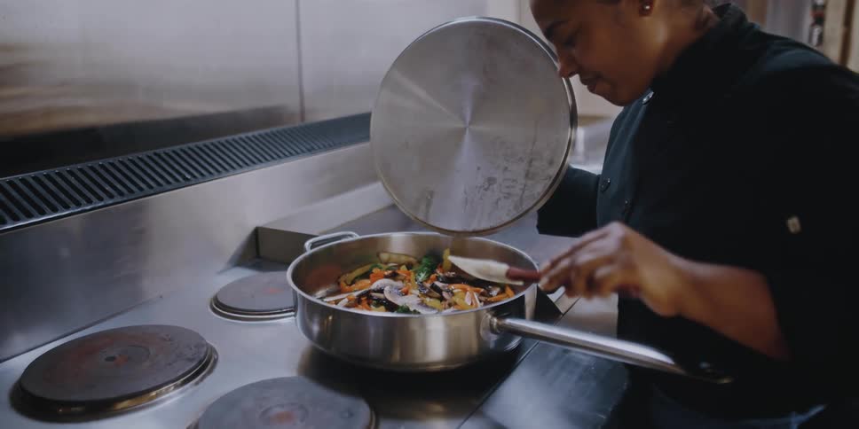 Female chef cooking vegetables on a pan in the kitchen of a restaurant