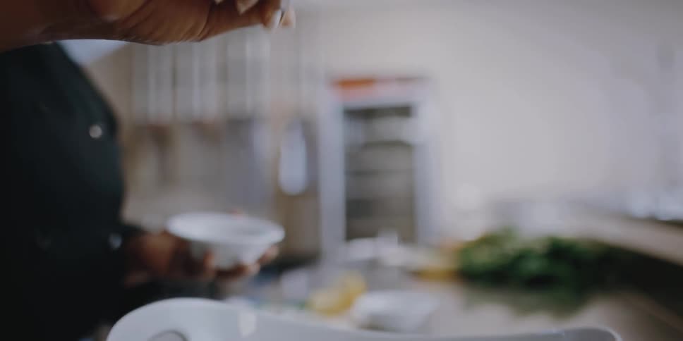 A female carefully sprinkles a topping over a freshly prepared dish containing pasta and vegetables