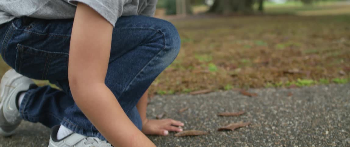 Boy crouches on asphalt drawing with blue chalk