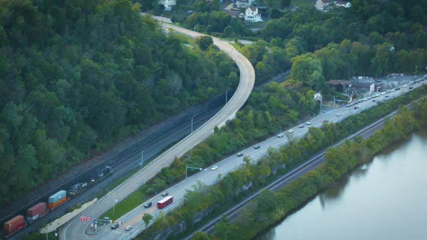 A road with vehicles next to a river with a bridge with the sky and clouds in the background