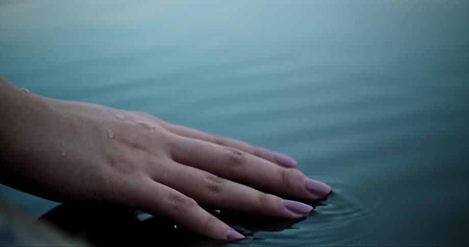 Hand touching the surface of the water causing ripples
