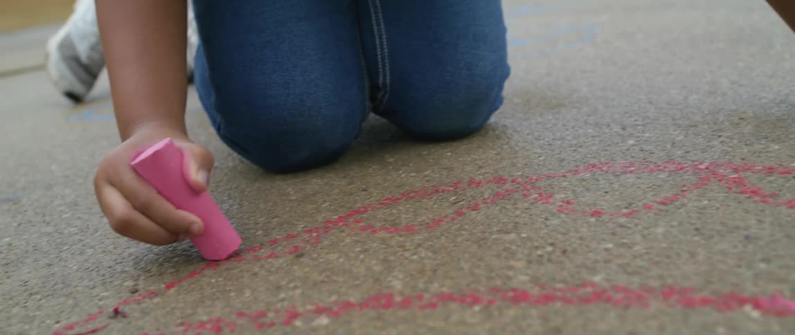 A girl drawing on the ground with pink chalk