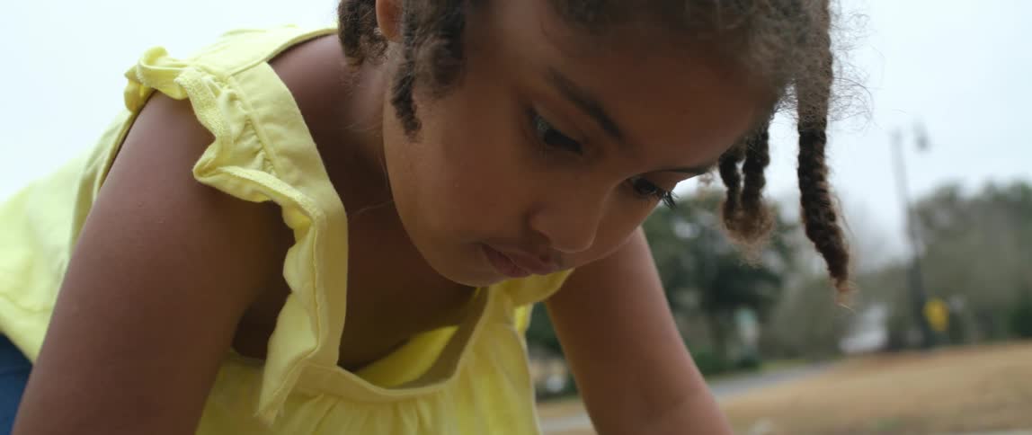 A child drawing a heart with pink chalk on the sidewalk