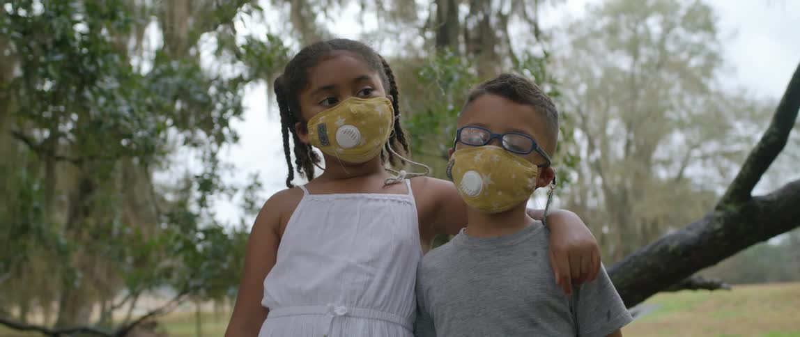 A boy and a girl wearing masks with trees the sky and clouds in the background