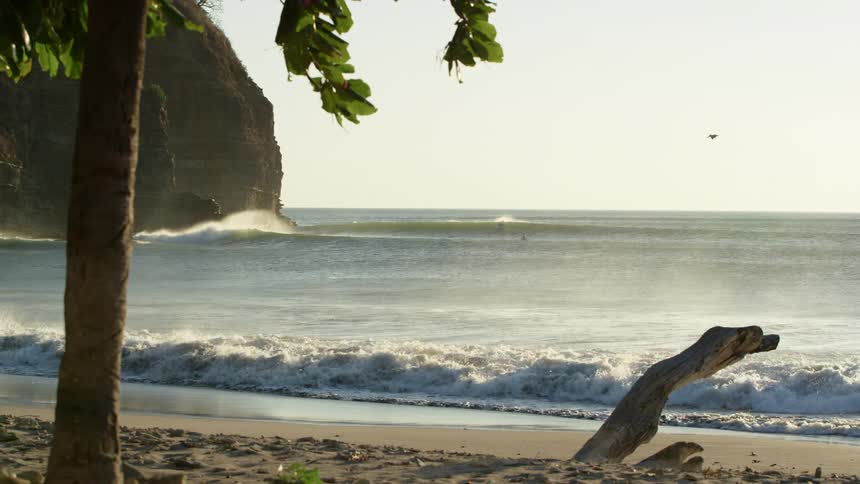Waves crashing on the white sand beach at sunset next to a cliff