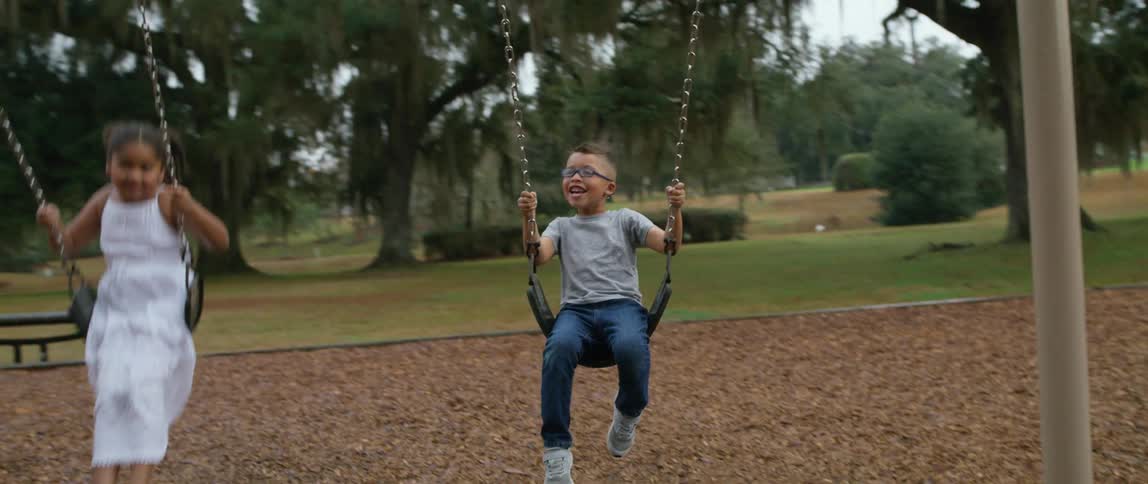 A boy and girl swing together at a playground