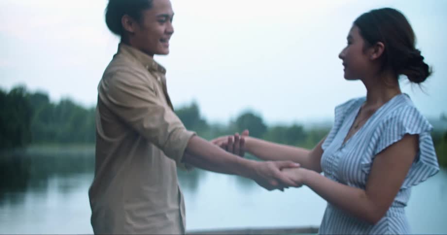 Couple holds hands and move in circle standing near lake