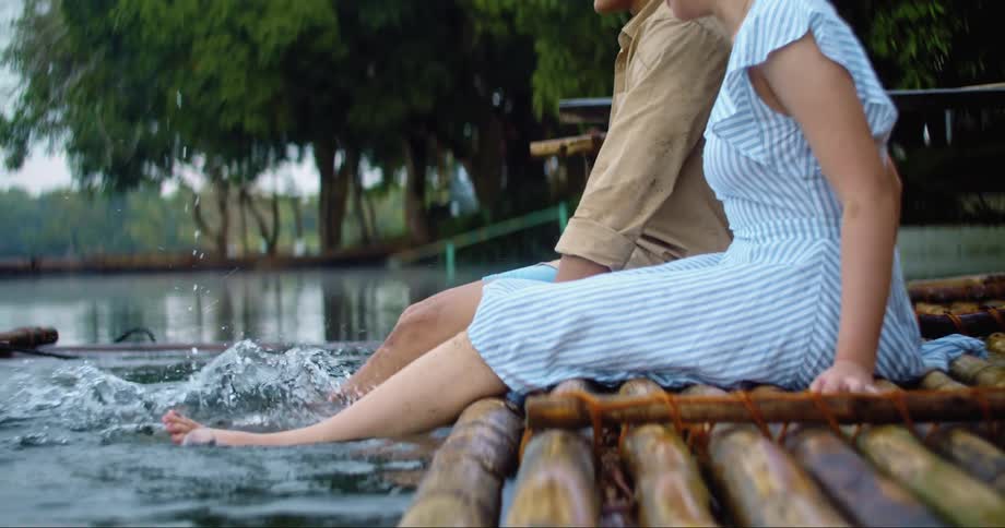 Woman and man sit side by side on a pier while kicking their feet in the water during the day