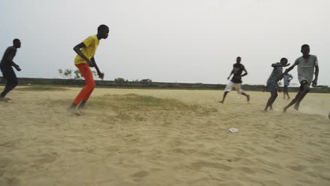 A group of boys running and playing soccer in a dirt field outside