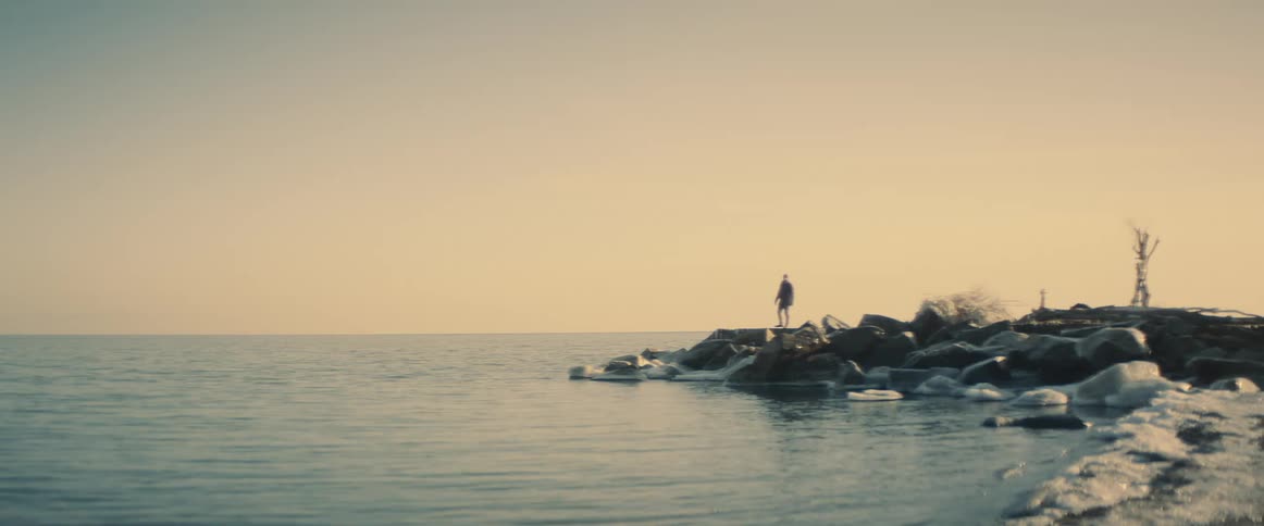 A man standing on the shore looks down at the water and then walks away