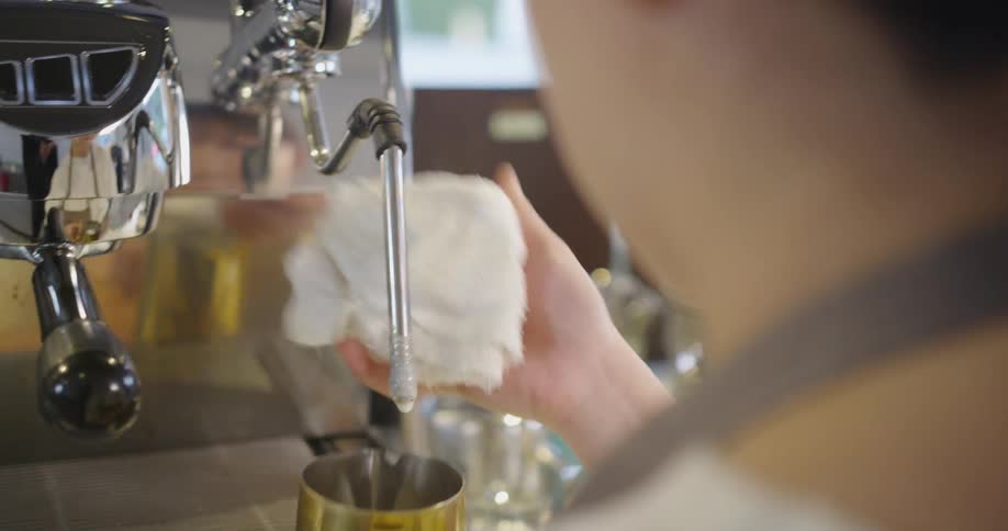 A woman with a apron in a coffee shop filling a cup with a espresso machine