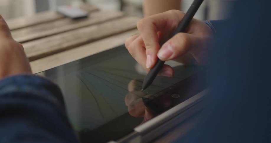 Person sketches on tablet sitting on wooden slat table with a stylus