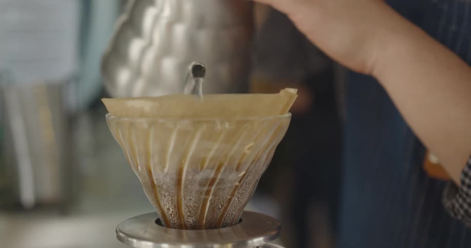Barista brews a pour over coffee by pouring hot water from metal coffee pot into glass pot