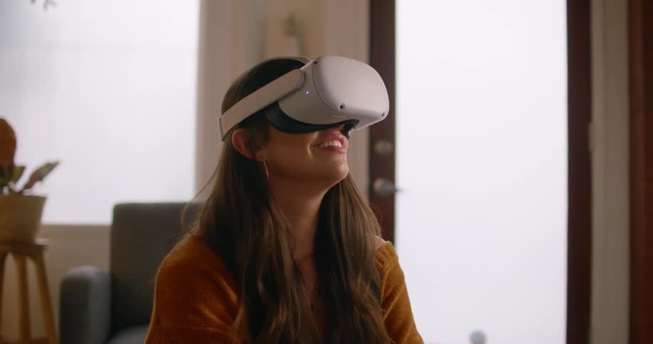 A woman in a room putting on a virtual reality headset with a chair and a door in the background