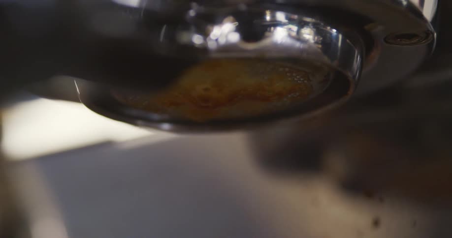 Espresso drips from the filter on an espresso machine into a cup