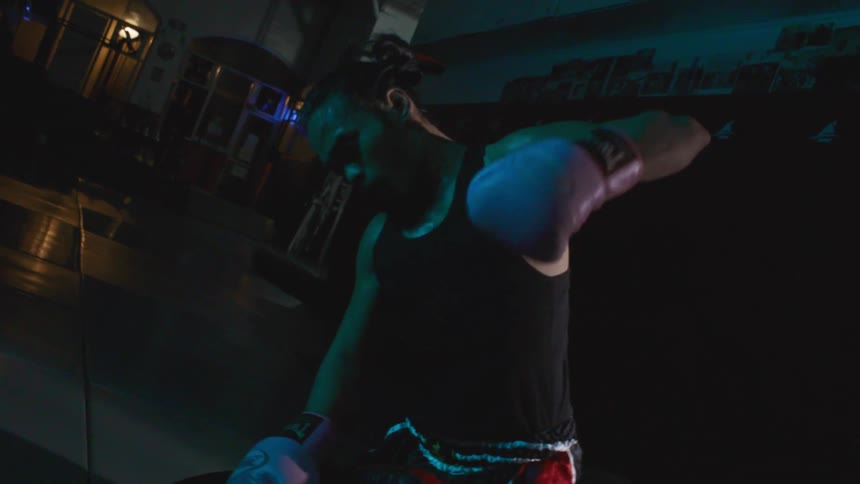 A man with boxing gloves punching and elbowing a dummy on the floor