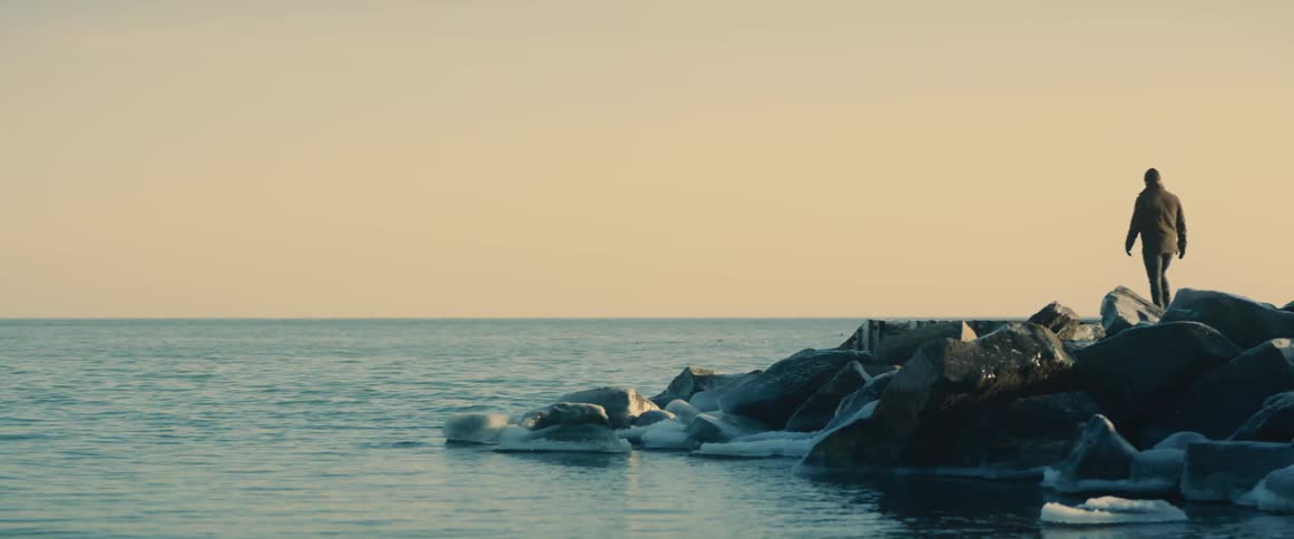 A man walking out on rocks near the ocean