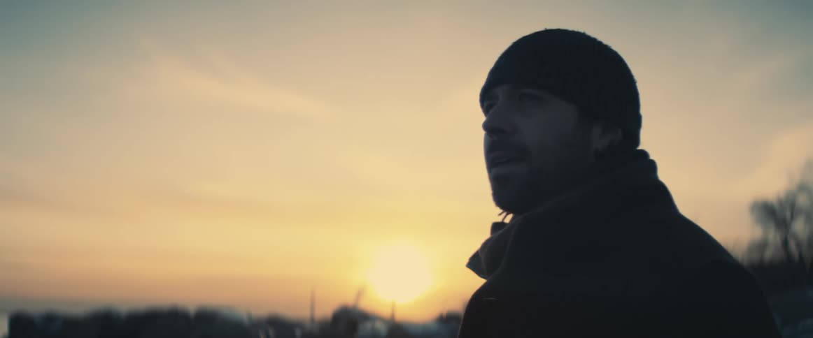 Man stands outside looking around as sun hovers just over horizon in red sky