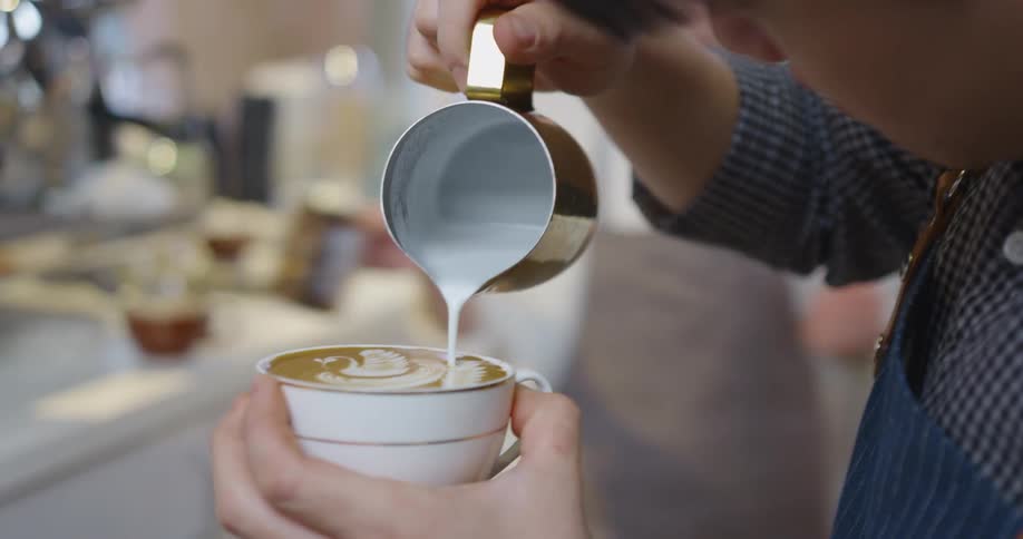 Two people are working in a coffee shop together while one is pouring latte art