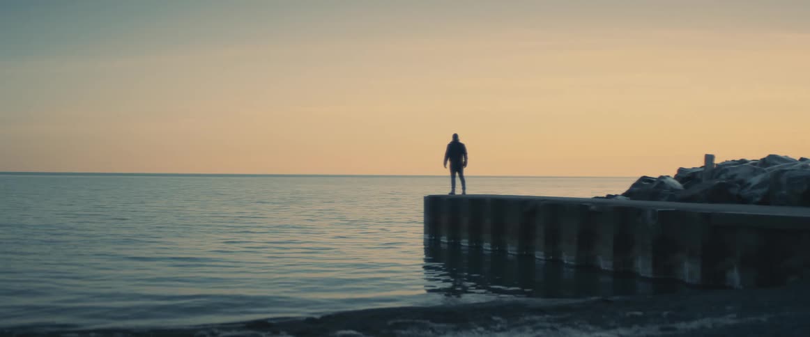 A lone man stands at the edge a dock overlooking a large body of water