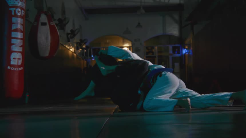 A pair of men practice grappling on the mats of a dimly lit gym