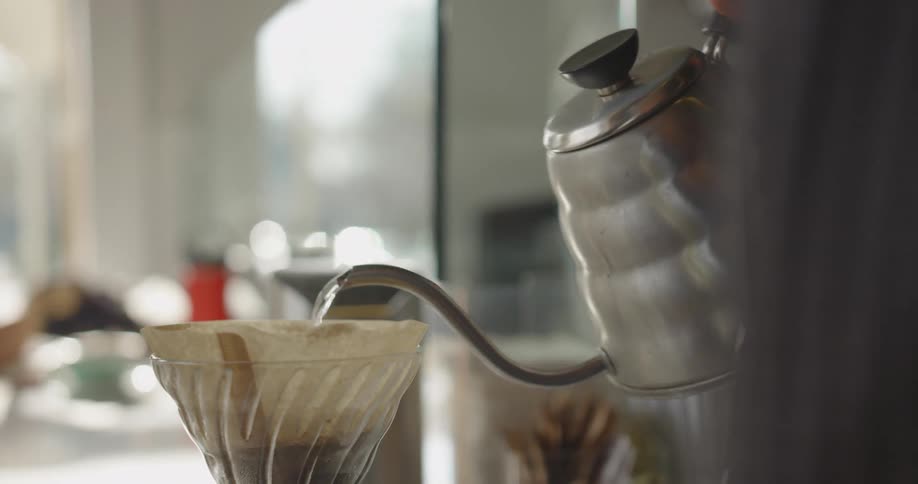 A barista makes a pour over with hot water from a kettle over coffee grounds in a filter funnel