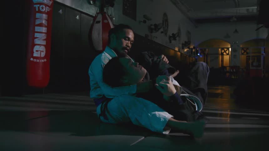 Two men in a room on a mat practicing martial arts with gi and belts
