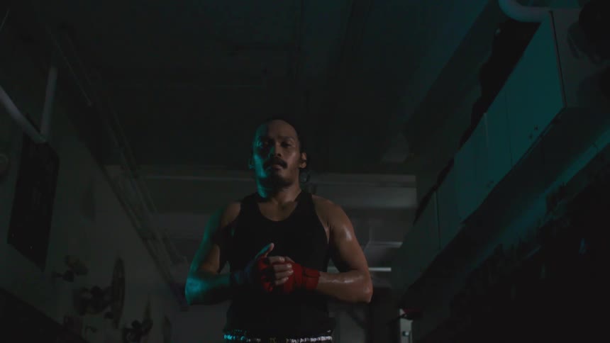 Boxer wearing half gloves stands in dimly lit building