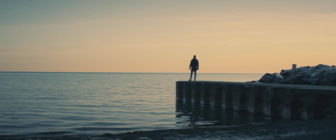 A person stands on a dock on the shore and looks out at the water