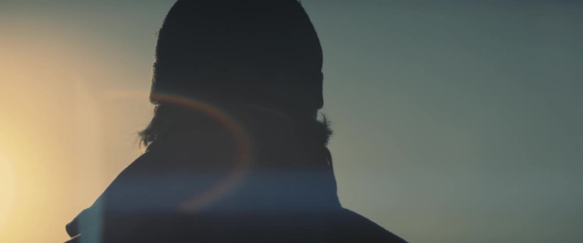 Man with a beanie and a coat is silhouetted against the sunlight at dusk