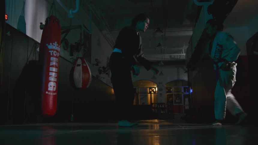 Two men in karate uniforms spar and wrestle in a gym