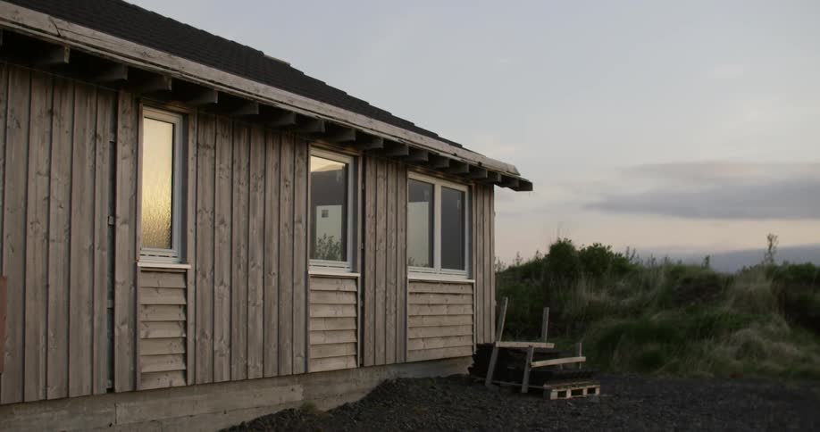 The sun is setting near a small home on a cloudy day