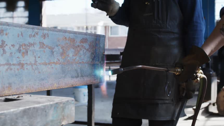 A person with gloves using a welding torch on a piece of metal in a warehouse