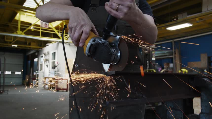 Sparks fly when a man cuts steel with a power tool inside a warehouse