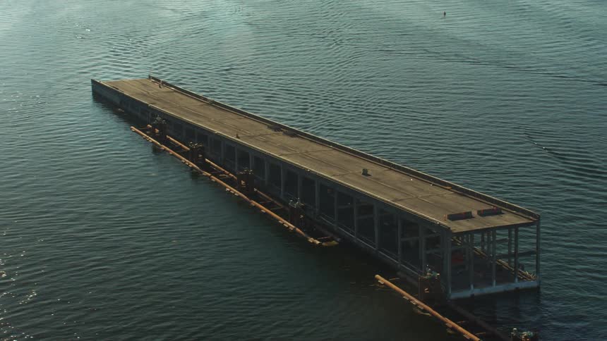 Sun glares off rippling water between unfinished bridge sections