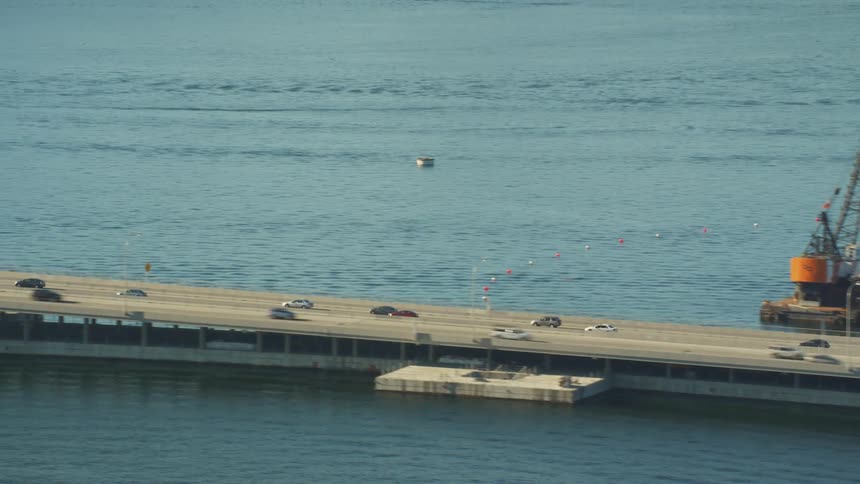Traffic travels along a long freeway over the ocean during the day